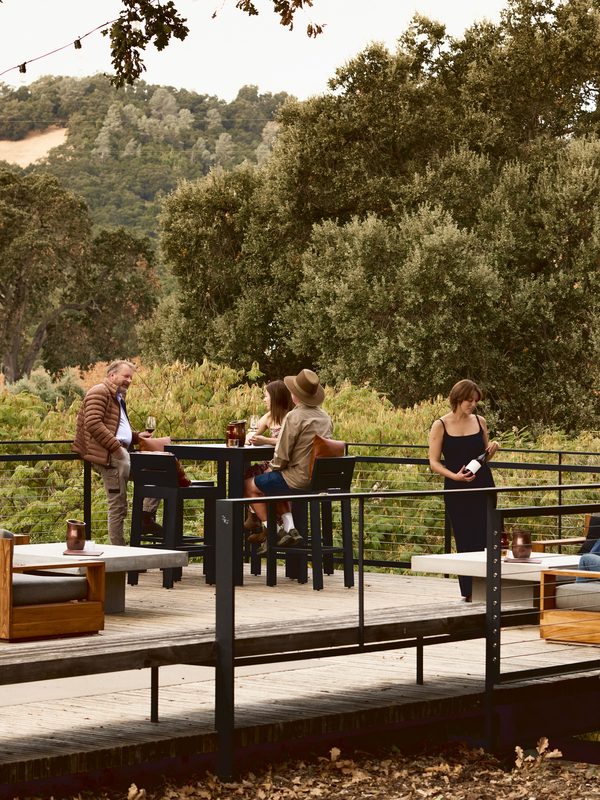 Guests enjoying wine on a spacious outdoor deck surrounded by lush trees and hills at Brecon Estate.
