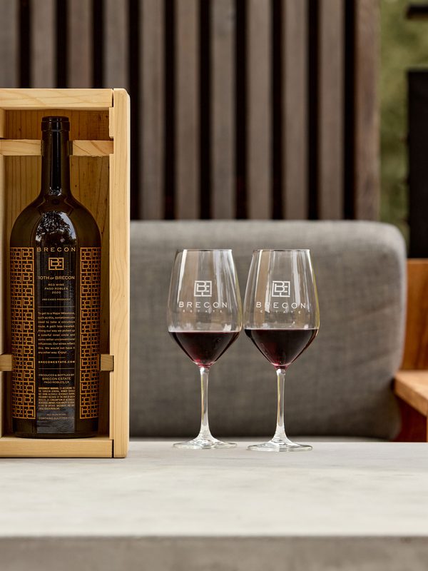 Large Brecon Estate wine bottle in an engraved wooden box beside two filled glasses on an outdoor table.